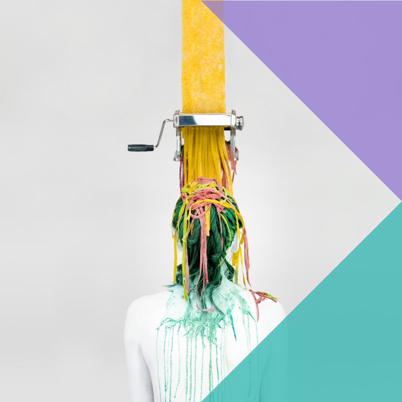 An abstract art image of pasta going into a pasta machine vertically from above and coming out the other end in various colours landing on a humanoid figure